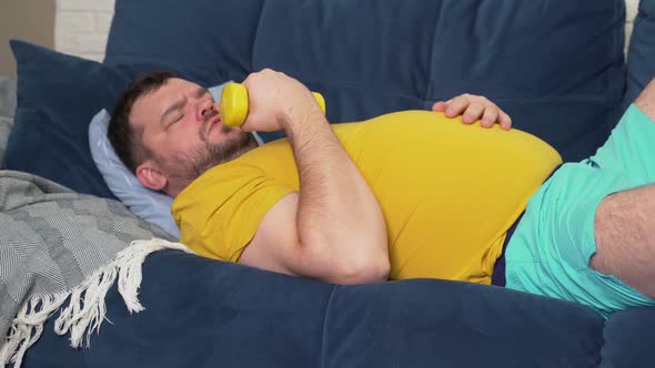 Funny Fat Man is Actively Engaged in Fitness with Yellow Small Dumbbells alt
