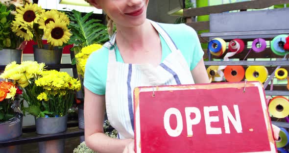 Smiling florist holding open sign on slate in flower shop alt