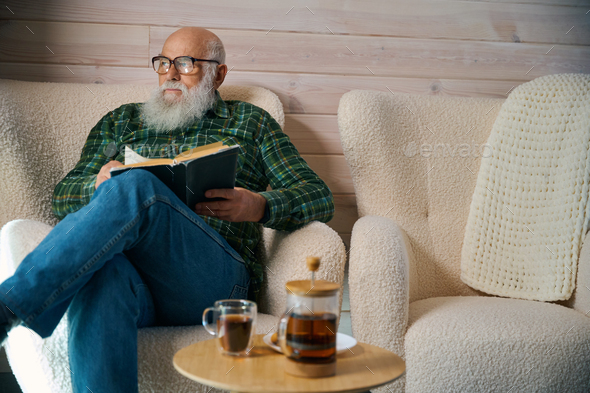 Old man with glasses settled down with book in comfortable chair