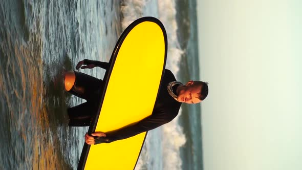 Guy in wetsuit with yellow surfboard is returning from surfing the waves. alt
