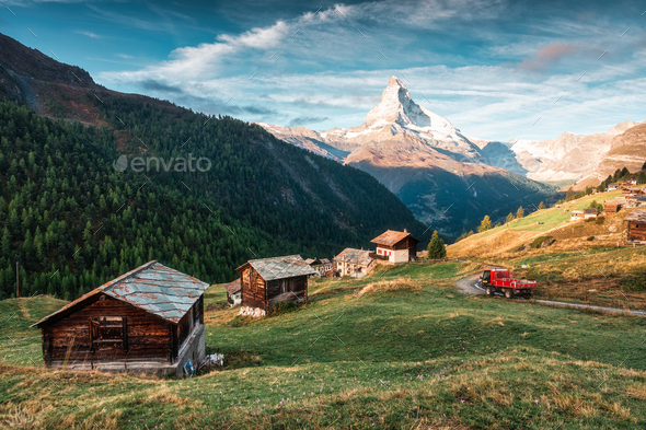 Matterhorn mountain with truck driving on the road and wooden huts on the hill in the morning