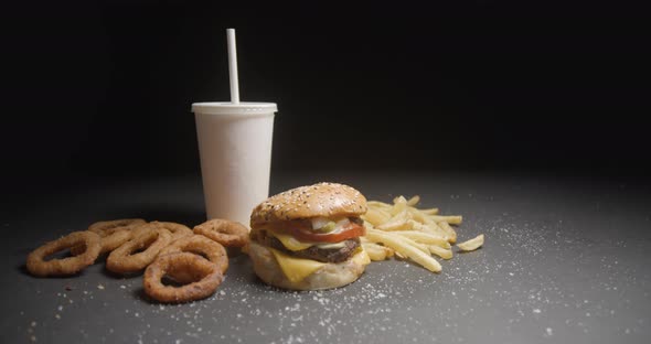 Fast food menu tracking shot in studio. Hamburger with french fries, onion rings and soda drink.