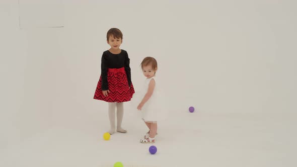 Toddler Girl Wearing Diaper and Her Sister Playing with Balls alt