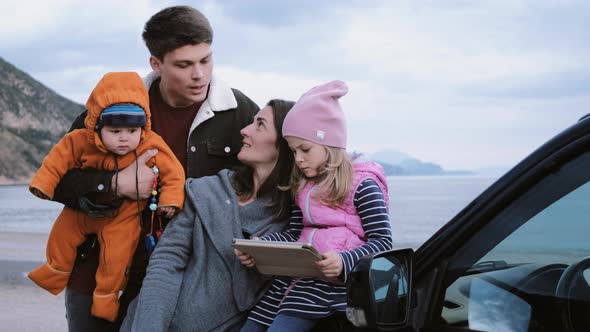 Family with children looking at a map on a tablet next to a car in nature. alt