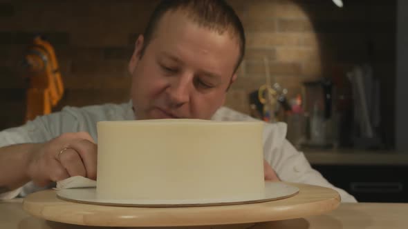 A Male Confectioner Perfectly Aligns a Cylindrical Biscuit Cake Covered with Cream By Rotating the alt