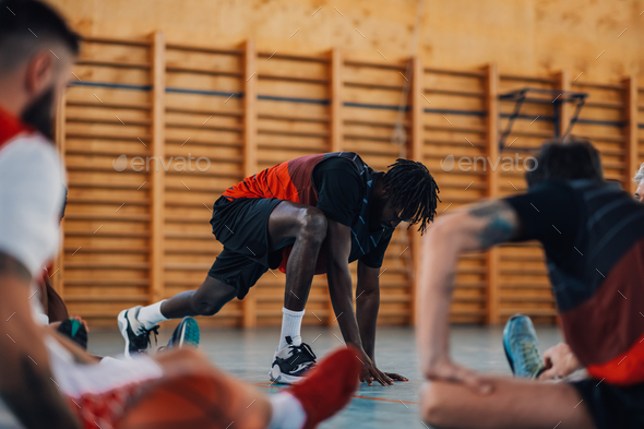 Interracial basketball players stretching legs on court during training ...