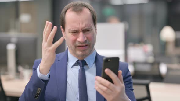 Portrait of Businessman Reacting to Loss on Smartphone alt