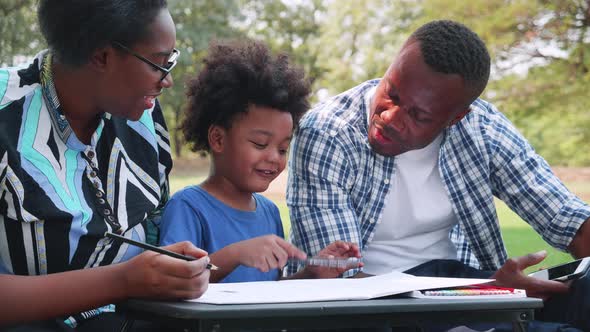 Young African couple relaxing with son to drawing during picnic in the park