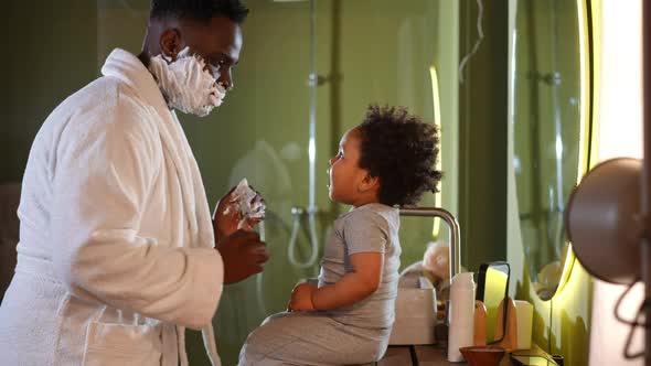 Side View Cute Little African American Boy Sitting in Bathroom with Father Shaving Playing with alt