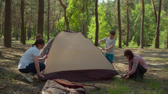 Two women and two boys having summer camping vacation in forest. Mothers and sons alt