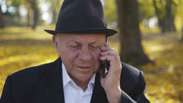 Handsome Senior Man Takes the Call and Talks on the Phone with a Smile alt