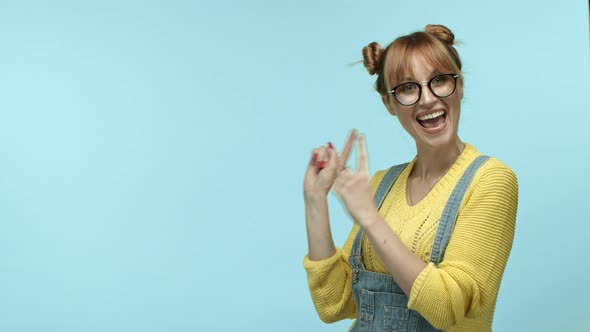Cheerful Girl Hipster in Glasses with Cute Bangs and Buns Hairstyle Pointing Fingers Left at Copy
