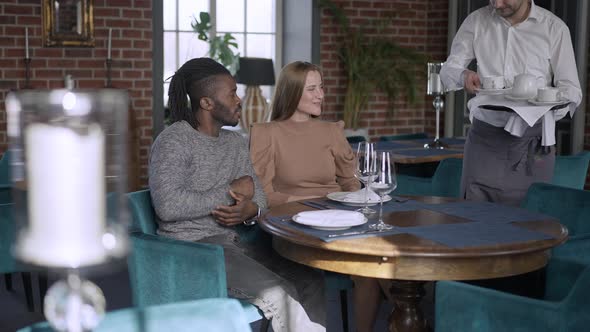Relaxed Carefree Couple Dating in Restaurant Talking As Waiter Bringing Afternoon Tea in Slow Motion alt