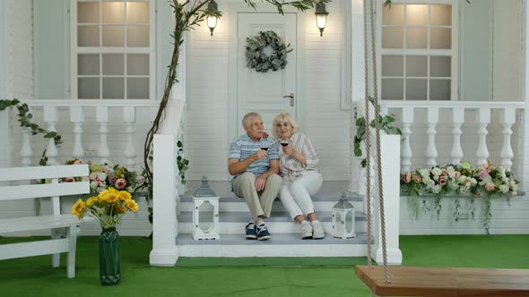 Satisfied Senior Elderly Caucasian Couple Sitting and Drinking Wine in Porch Stairs at Home alt