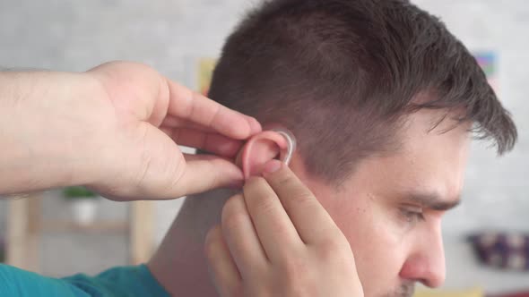 Man Inserts a Hearing Aid Into Her Ear alt