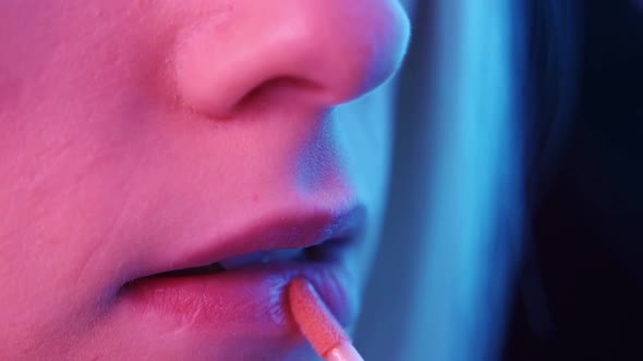 Woman Paints Her Lips in Colored Lighting on a Black Background