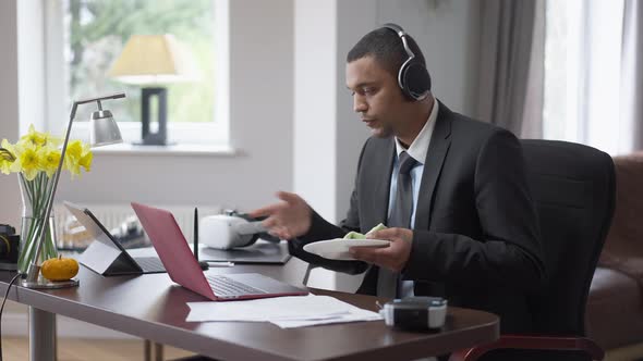 Young African American Man in Suit and Headphones Sitting in Home Office Talking in Video Chat and alt