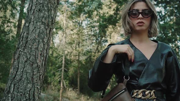 A beautiful woman with stylish sun glasses and earings walks towards the camera wearing trendy jacke alt