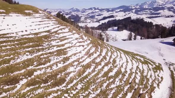 Drone flies over a hill so that a lot of others mountains gets visible. There is also a lodge under alt