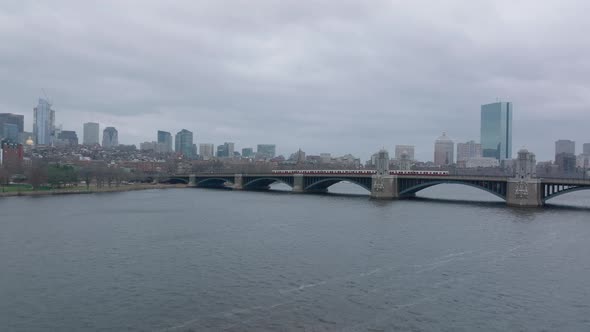 Red Line Train Driving on Longfellow Bridge with Urban Borough in Background alt