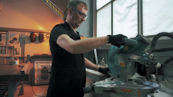 Factory worker saws a metal part with a circular saw