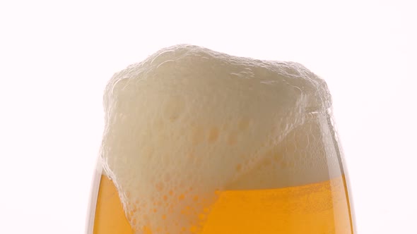 Glass of beer with froth in slow motion on white background