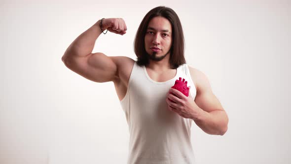 Caucasian Muscular Man with Long Dark Hair and Beard Pumping Fake Anatomical Heart in One Hand and alt