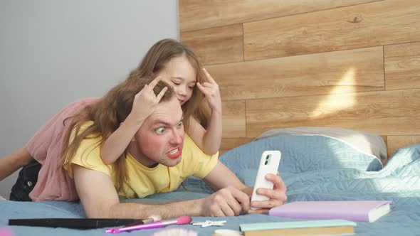 Happy Little Daughter and Smiling Father with Makeup on Face Taking Selfie with Smartphone at Home