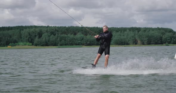 Wakeboarding on the Lake Near Forest, Sportsman Surfs on Water and Does a Somersault, Ride on alt