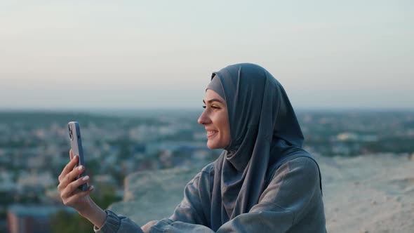 Beautiful Woman in Hijab on Top of the Hill in the Evening Has Videocall By Smartphone