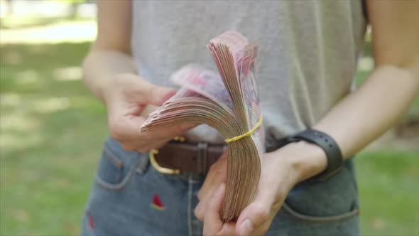 A Woman is Holding a Thick Wad of Cash in Her Hands and Counting It in Slow Motion