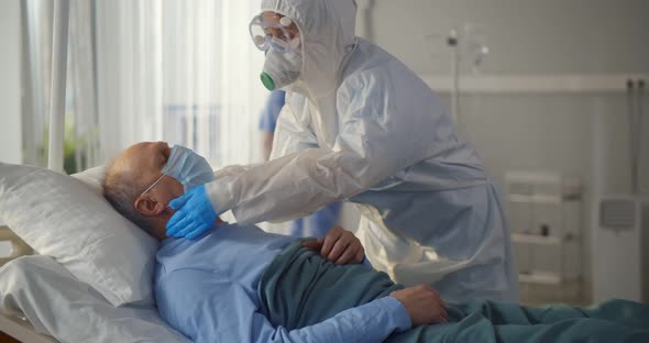 Nurse Putting Oxygen Mask on Elderly Man Patient Lying in Hospital Room Bed alt