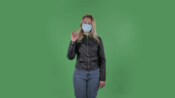 Portrait of Beautiful Young Woman in Medical Mask Is Looking Straight Sighs Relieved and Making Sign alt