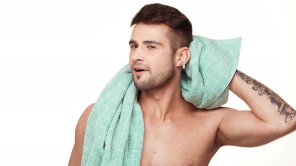 Positive Caucasian Topless Male with Tattoed Hand Wiping Head with a Towel Around His Neck Standing alt