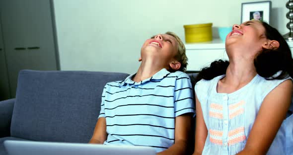 Siblings having fun on sofa in living room alt