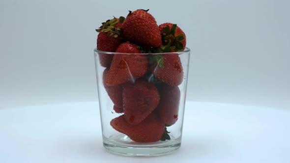 Strawberries in a clear glass rotating on a white background. Strawberry ripe season