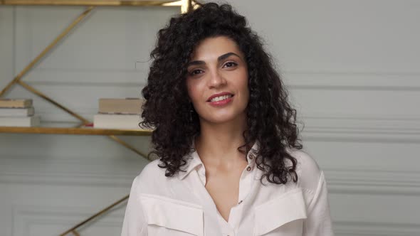 Portrait of a Cheerful Young Mixedrace Woman with Curly Hair in a White Shirt Posing and Looking at alt