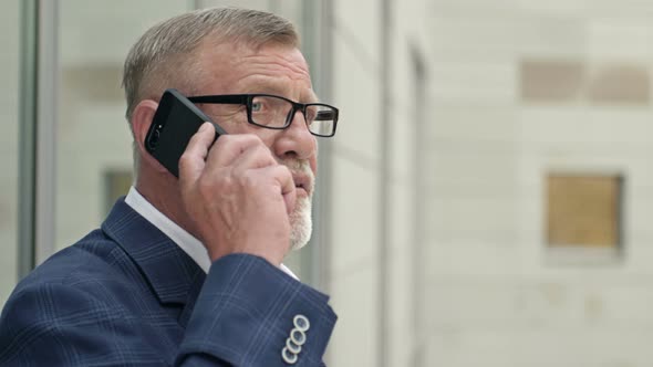 Portrait of a Senior Businessman Talking with a Smart Phone Outside of Modern Office Building alt