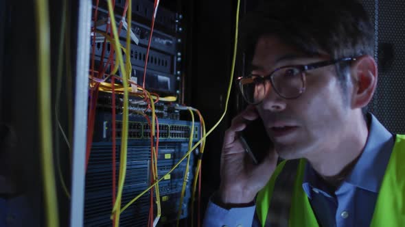 Asian male it technician using smartphone checking computer server alt