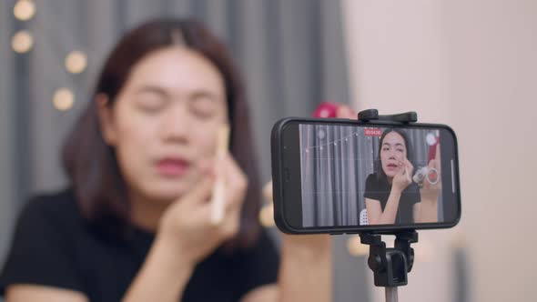 Asian woman beauty blogger influencer makeup artist recording on smartphone.