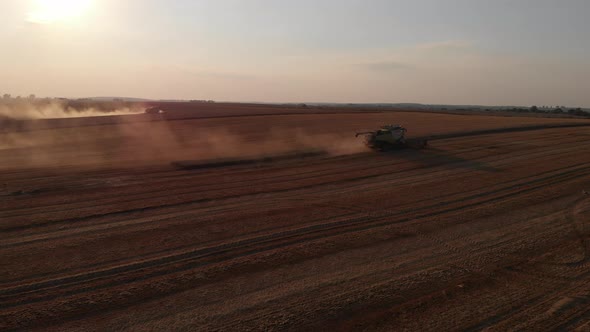 Aerial shot: fly along combines harvesting at sunset