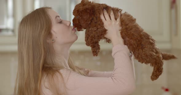 A poodle puppy licks the face of a young beautiful girl while she holds it in front of her face