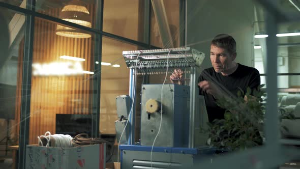 An employee of a weaving factory maintains a machine for weaving ropes and cords from yarns