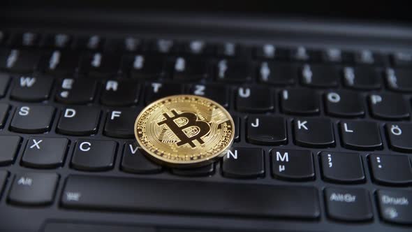 Closeup of a golden bitcoin medal on a black keyboard.