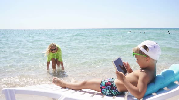 Mother Looks at Her Son Who Is Resting on a Sun Lounger on the Beach By the Water alt
