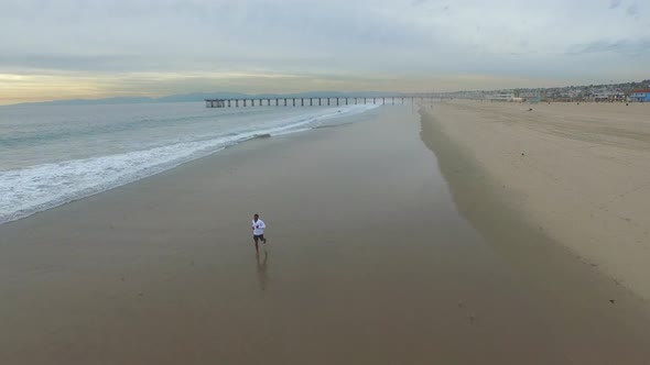 Aerial shot of young man running on the beach. alt