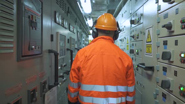 Electrician Walks Down Corridor Between Electrical Panels