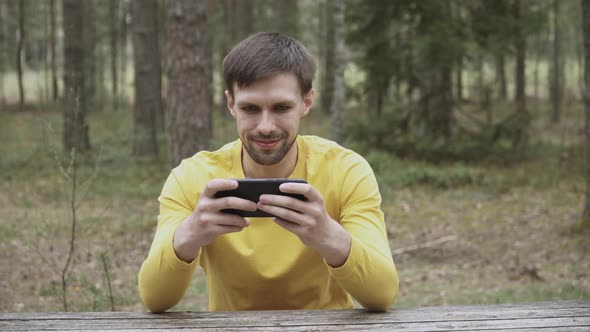 Guy with Stubble is Satisfied with Process of Successful Mobile Game on Phone alt