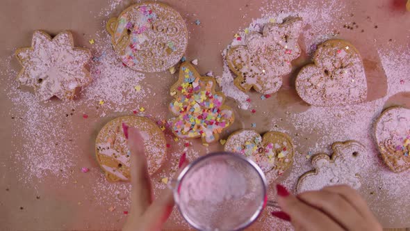 Female Hands Sprinkle Powdered Sugar on Christmas Cookies with Sieve Top View