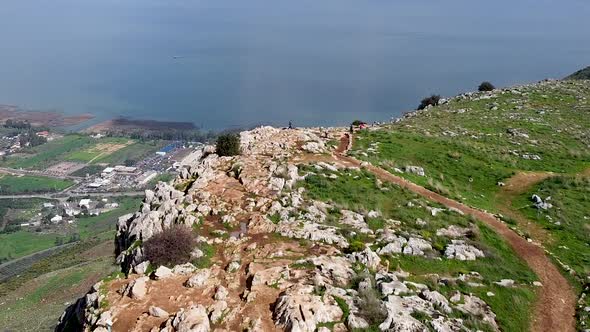 Aerial forward shot of few people on a mud trail at the Arbel cliff, Galilee sea with sun rays in th alt